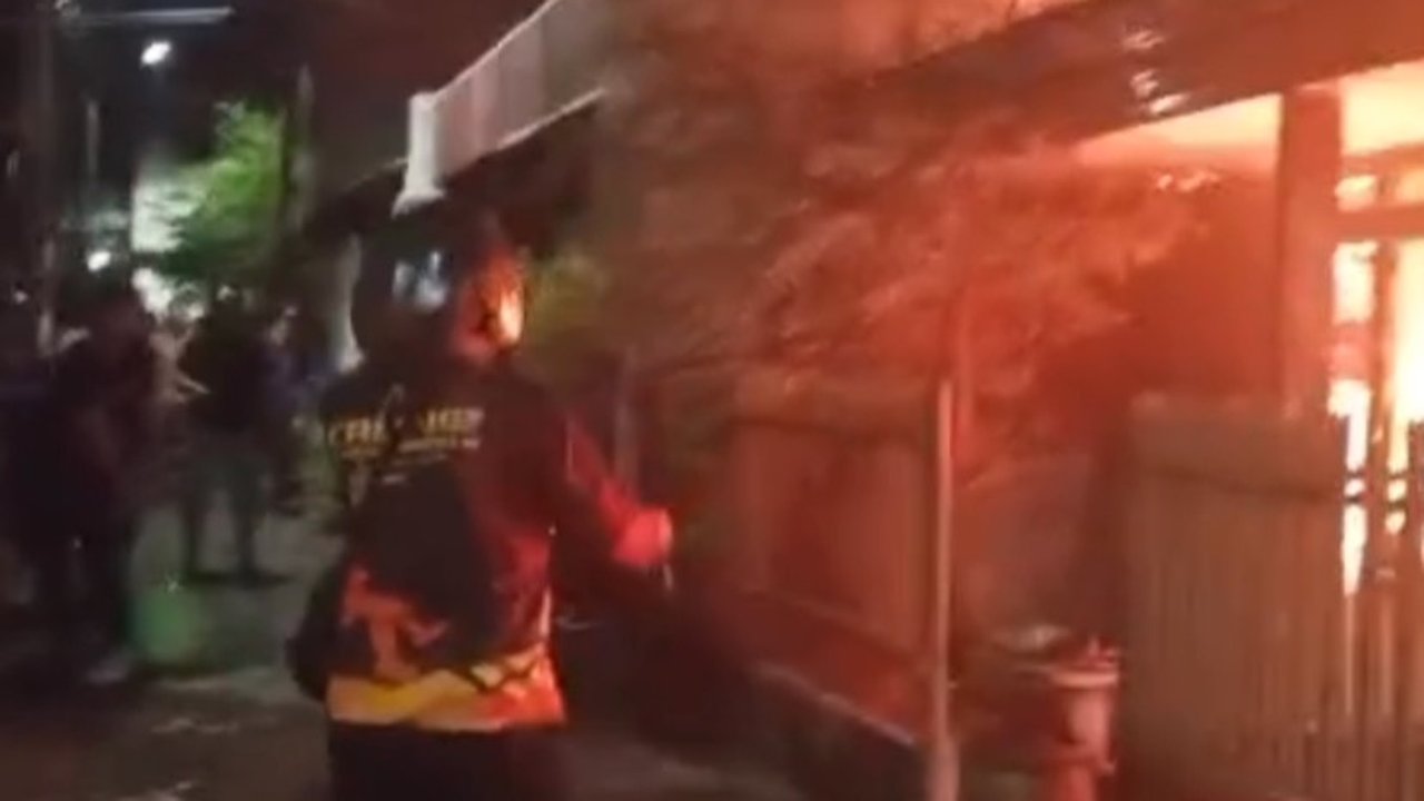 Api membesar dari atap rumah di Jalan Ambengan Batu Surabaya pada malam hari dan petugas pemadam terlihat di lokasi.