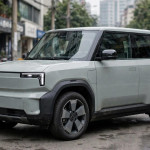 Ilustrasi SUV listrik kompak bergaya Honda 0 Alpha dengan bodi kotak dan buritan tegak di jalan kota.