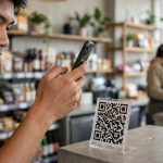 Seorang pembeli memindai papan kode QR di kasir sebuah kafe modern.
