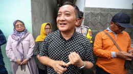 Seorang pria berbicara di sebuah gang di kawasan Kedung Anyar, Sawahan, disaksikan warga dan petugas kepolisian.