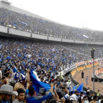 Suporter memadati tribun stadion sepak bola.